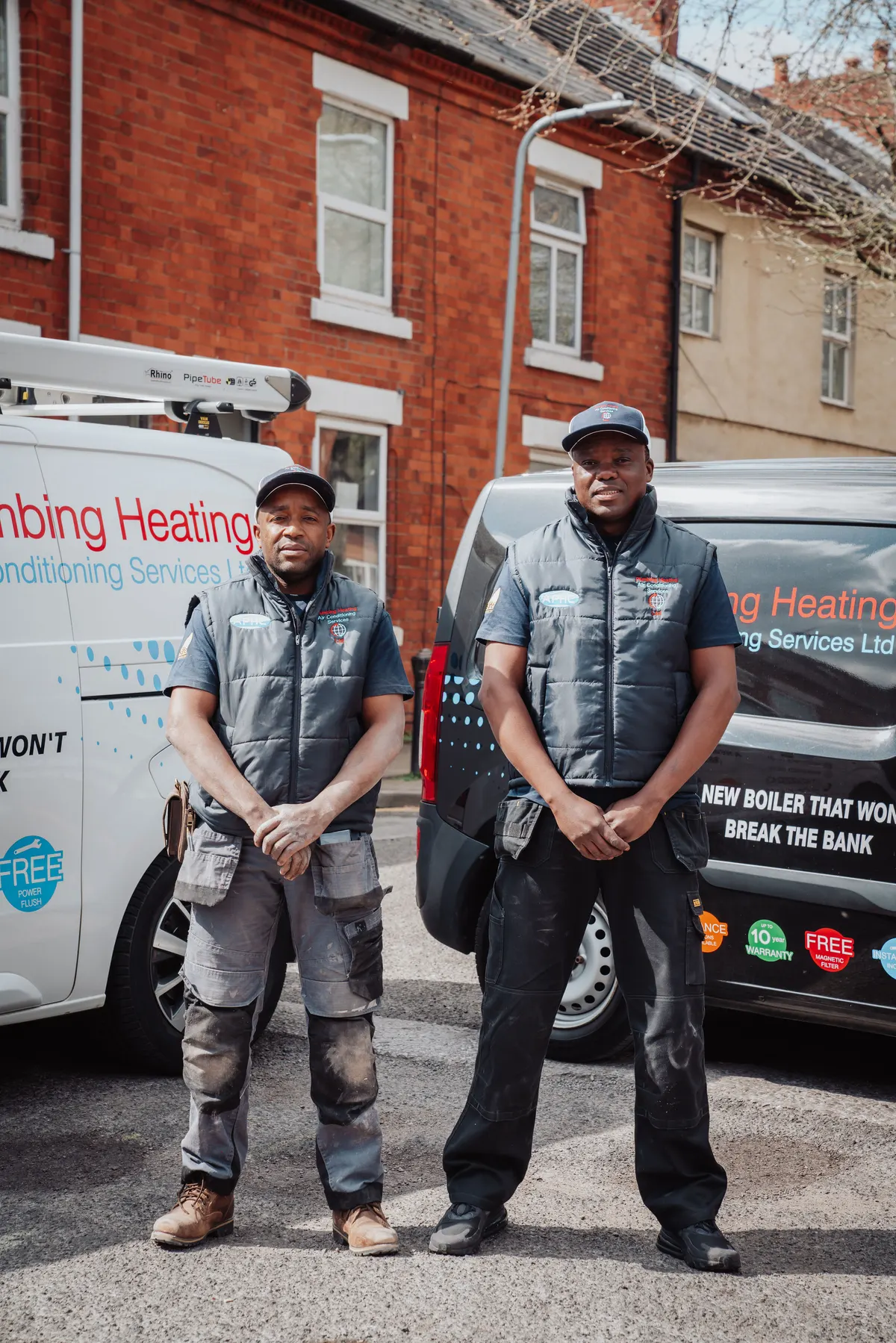 Two PHACS engineers in branded workwear standing beside their liveried vans in Coalville